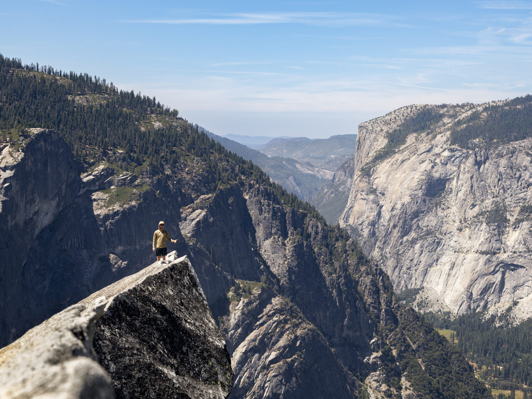 A tiny figure giving a thumbs up on a granite ledge overlooking El Capitan, Yosemite
